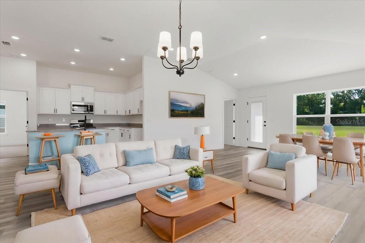 Spacious open concept living area featuring a modern kitchen with white cabinetry, a living room with a neutral sofa and armchairs, and a dining space with light wood furniture.