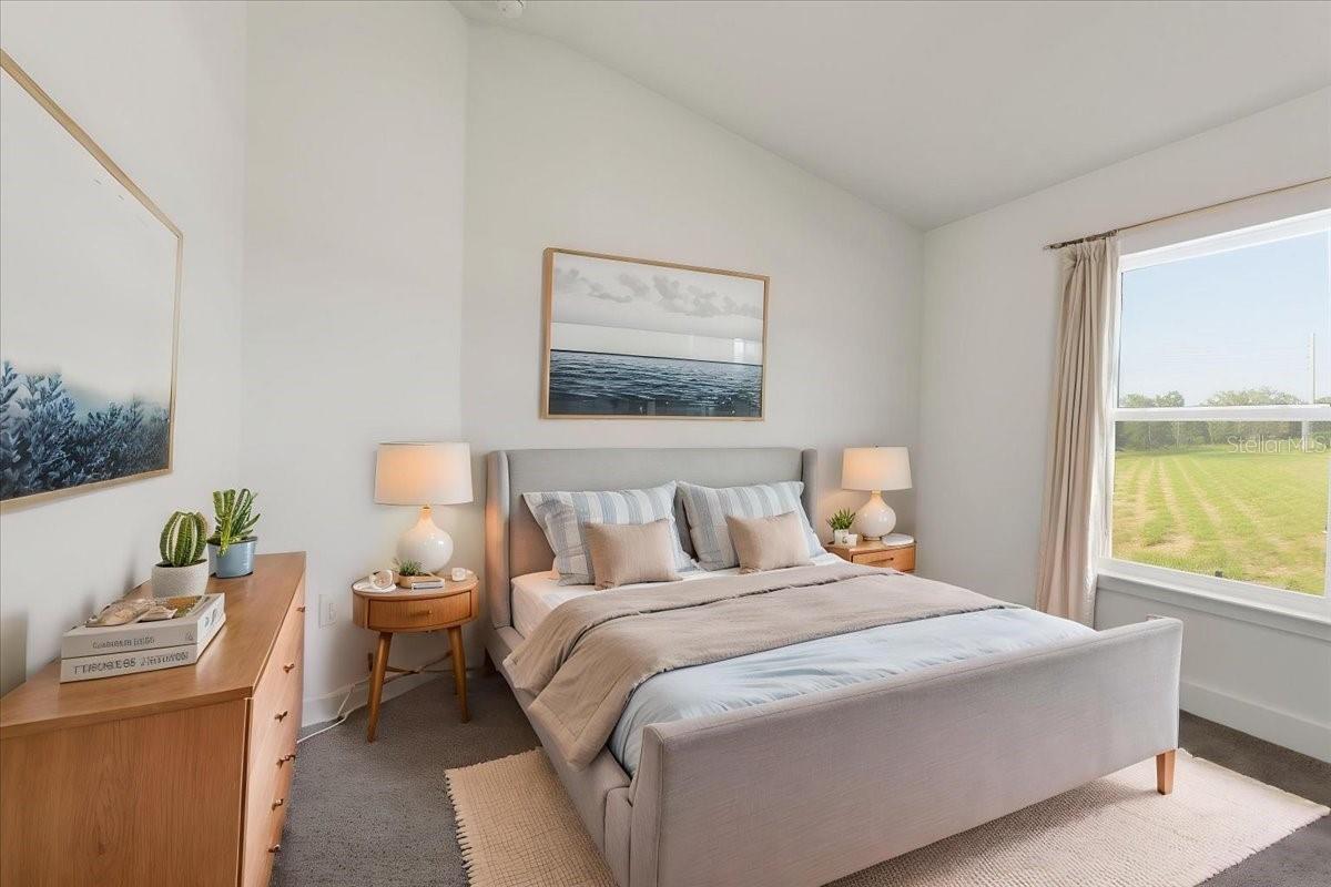 Modern bedroom with light grey upholstered bed, natural wood nightstands, and a window overlooking a grassy field.