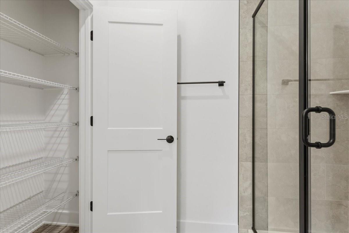 A white door leading to a walk-in closet next to a walk-in shower with black trim in a modern bathroom.