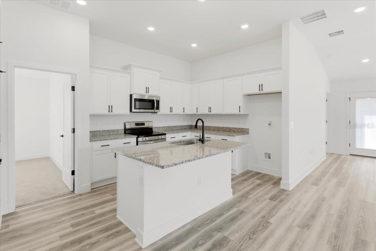 A modern kitchen with white cabinets, granite countertops, an island, and light wood flooring.