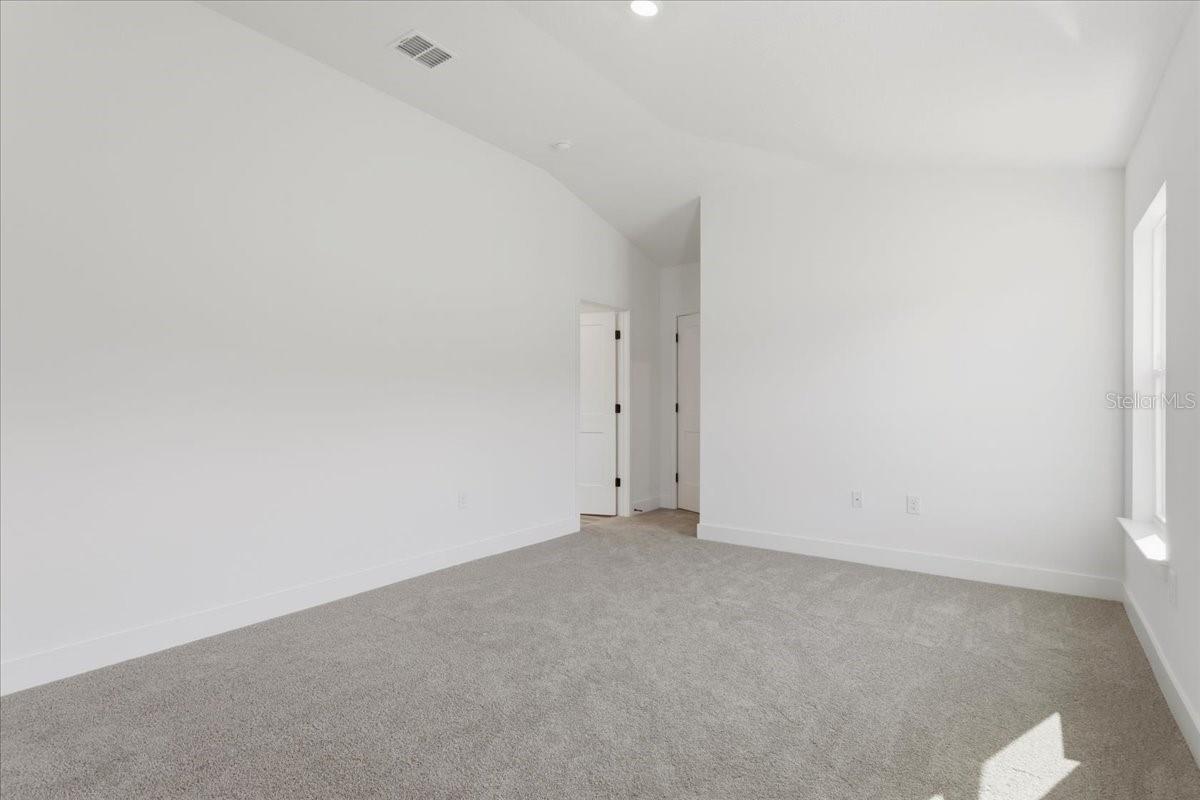 An empty bedroom with gray carpet, white walls, vaulted ceiling, and white interior doors.