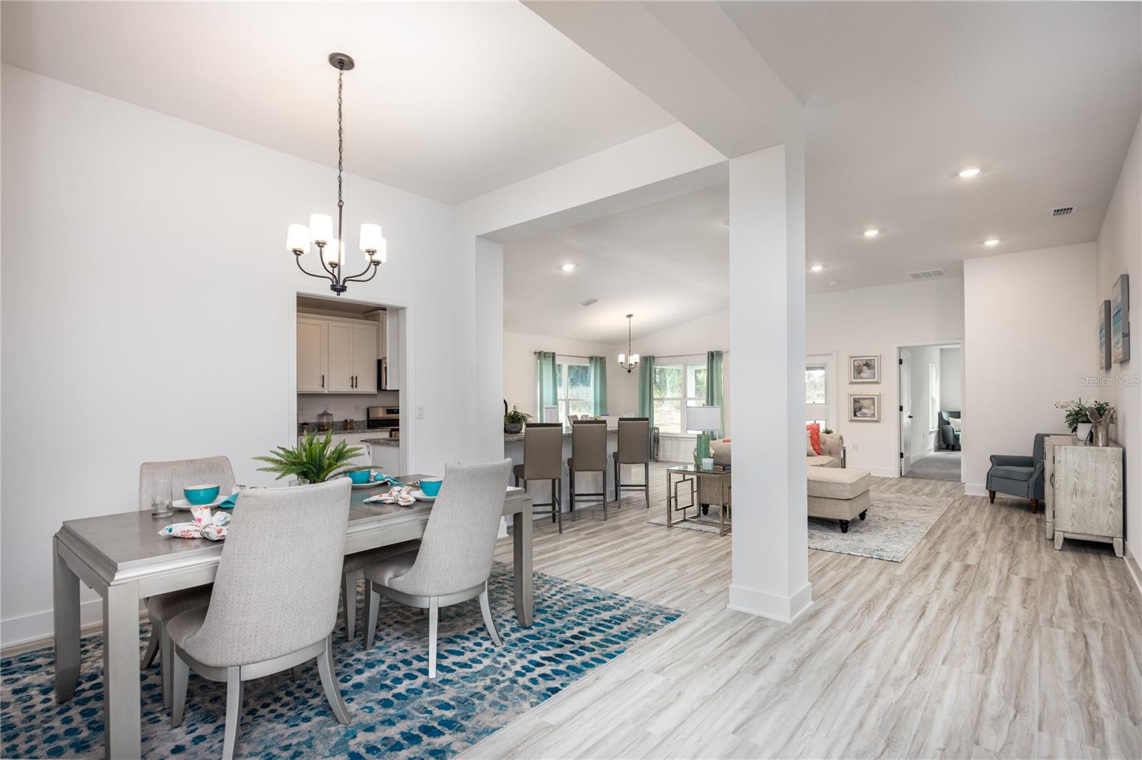 A dining area with a modern table and chairs leads into an open concept kitchen and living area with wood-look flooring.