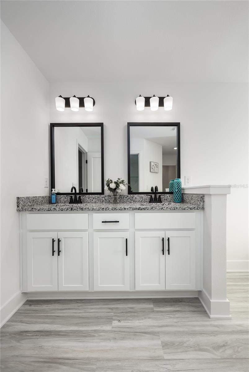 A modern bathroom vanity with dual sinks, white cabinetry, granite countertops, and black framed mirrors.