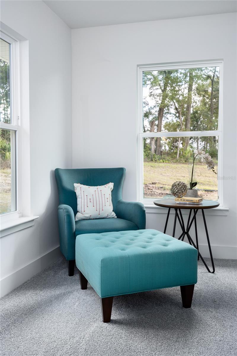 A teal armchair and matching tufted ottoman in a bright corner sitting area with large windows.