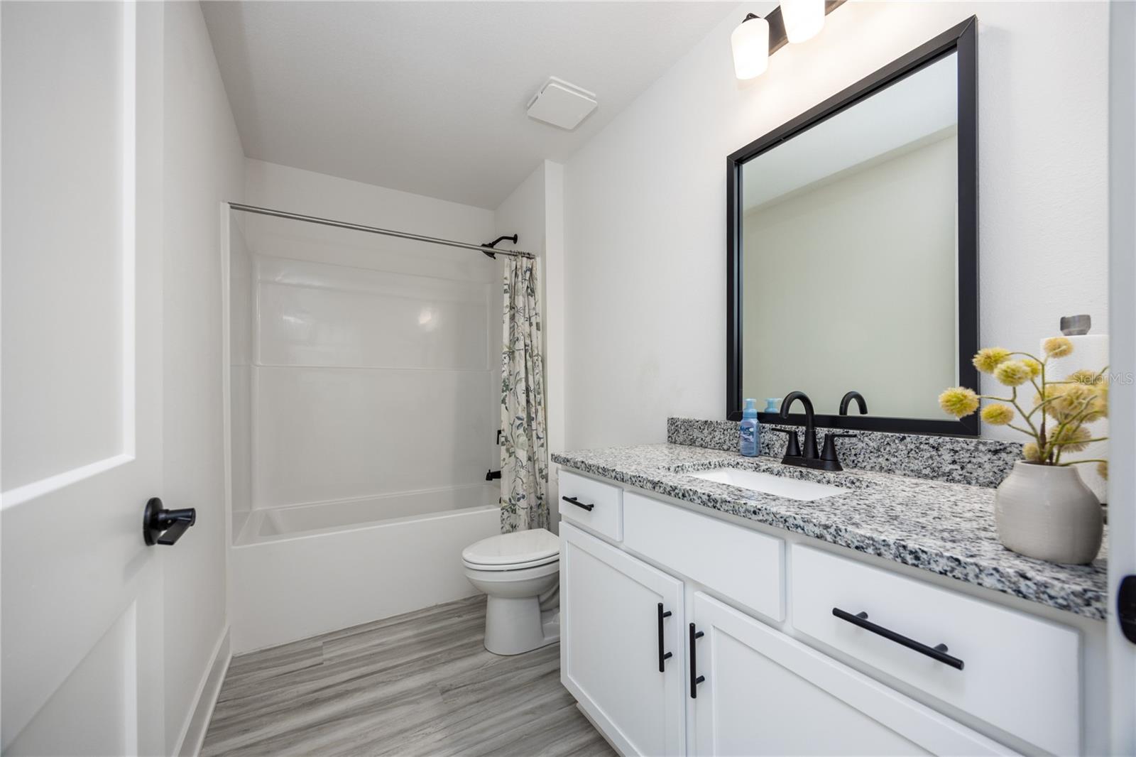 A modern bathroom with white vanity cabinets, granite countertops, and a shower-tub combo.