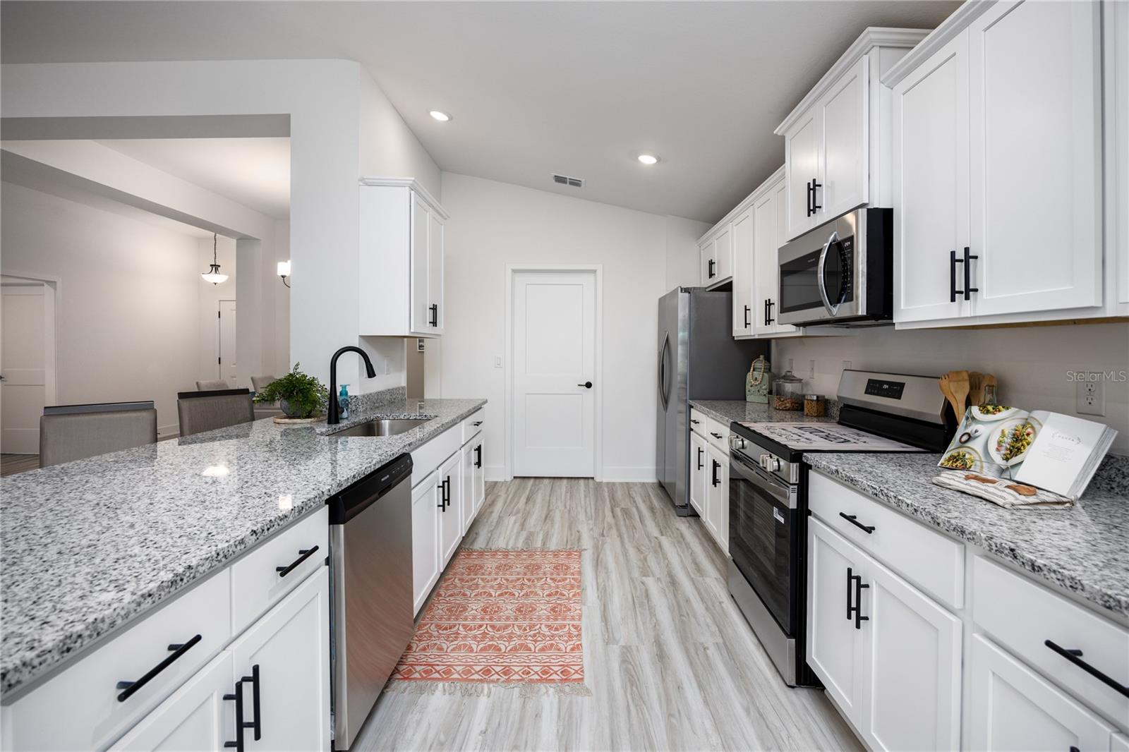 A clean, modern galley kitchen featuring white cabinets, granite countertops, and stainless steel appliances.
