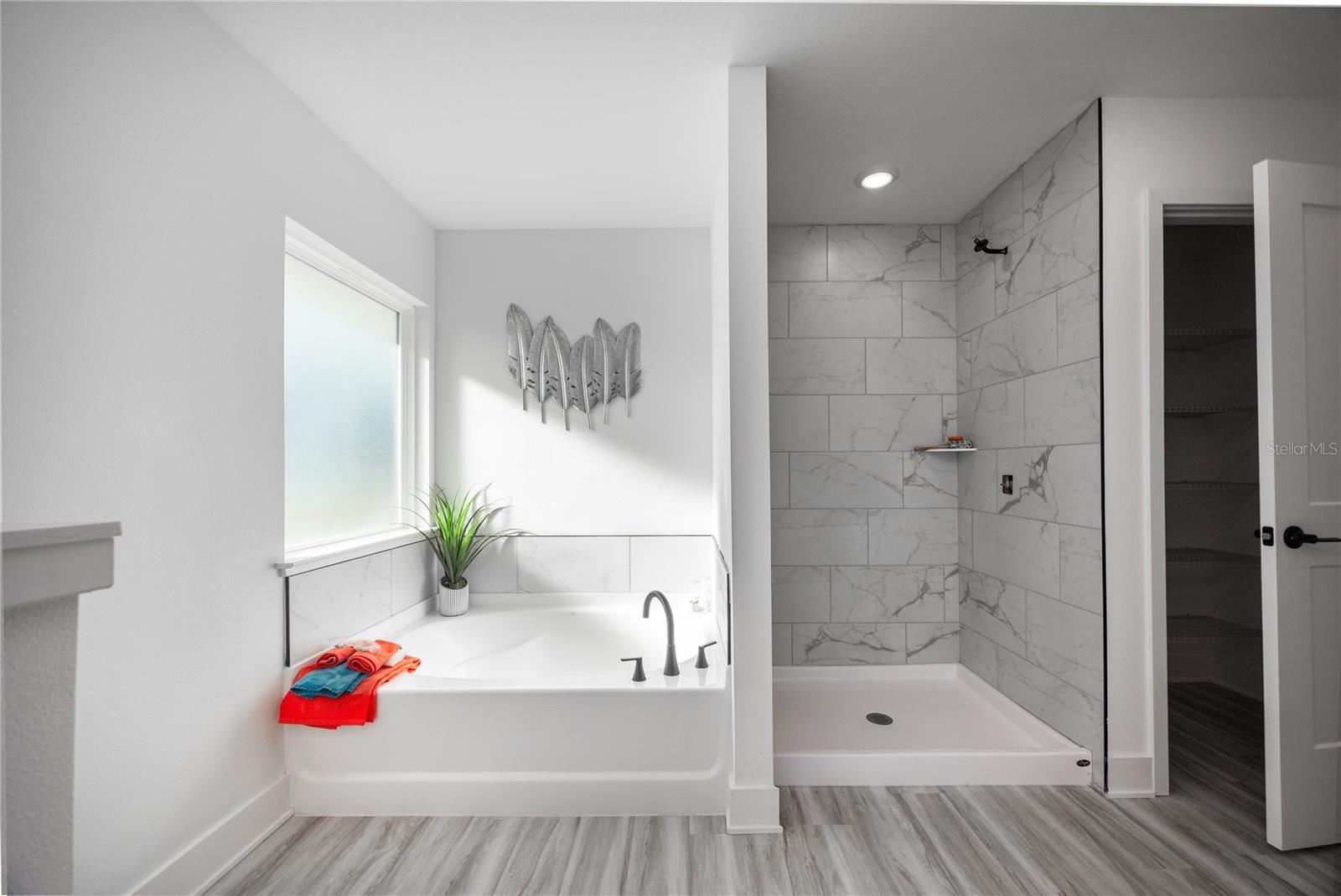 Modern primary bathroom featuring a soaking tub under a window and a walk-in shower with marble-look tile walls