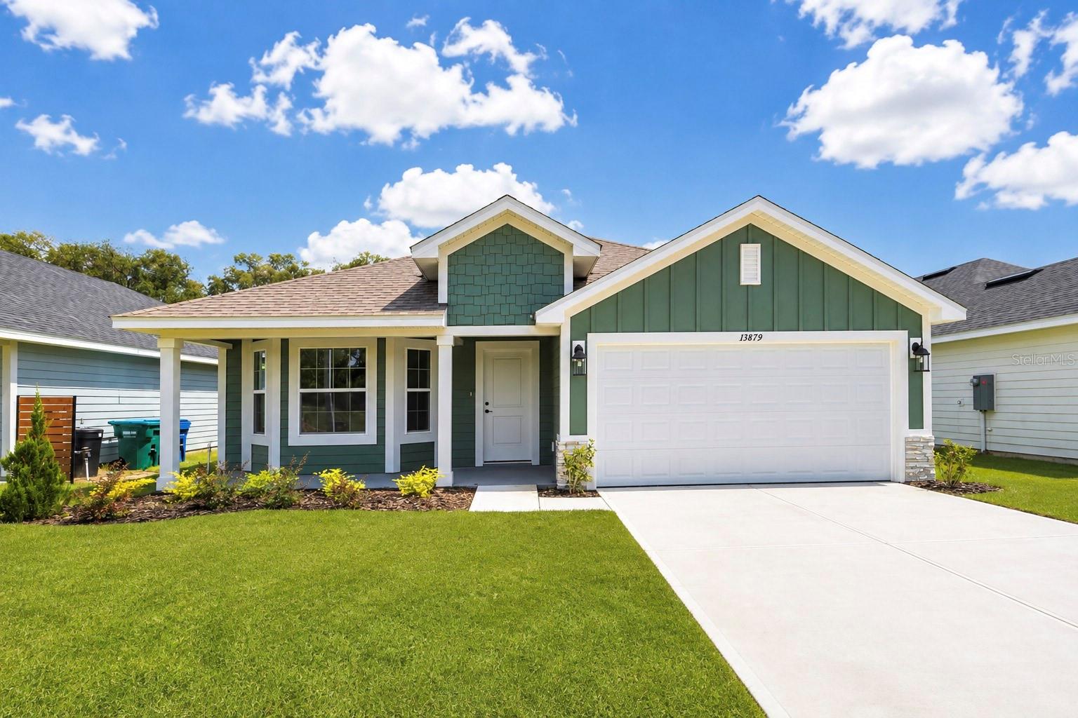 Front exterior view of a green house with a white garage door and a grassy lawn under a blue sky.