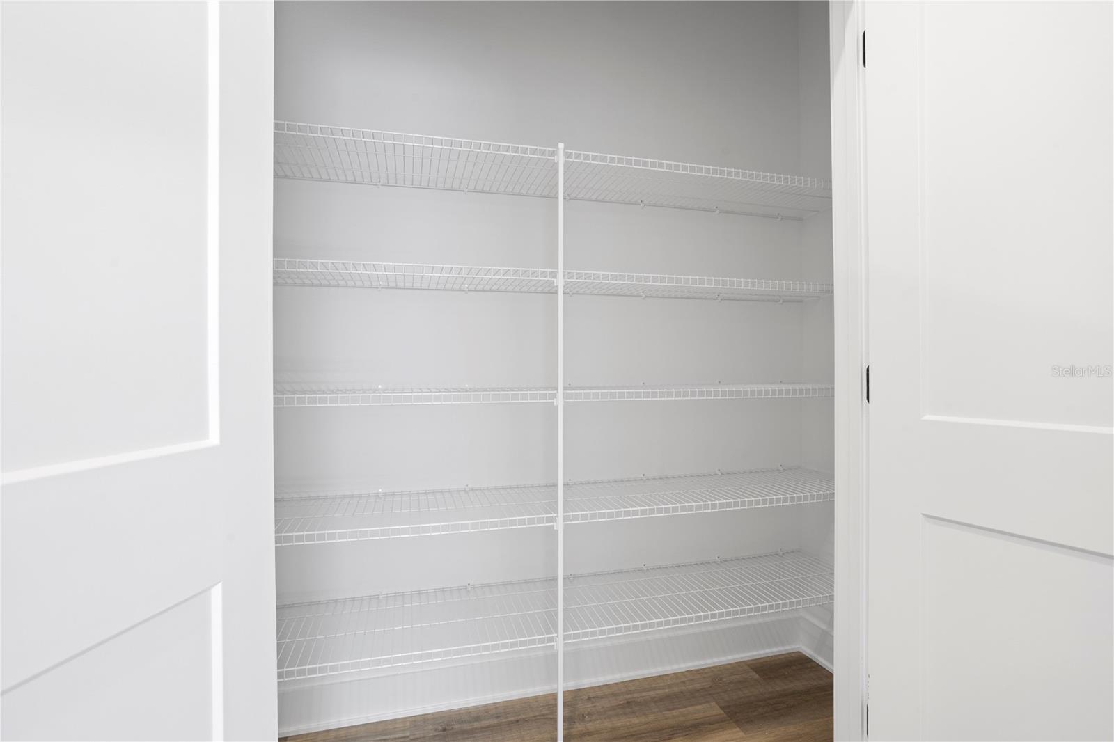 An empty reach-in pantry with white wire shelving units and wood-look laminate flooring.
