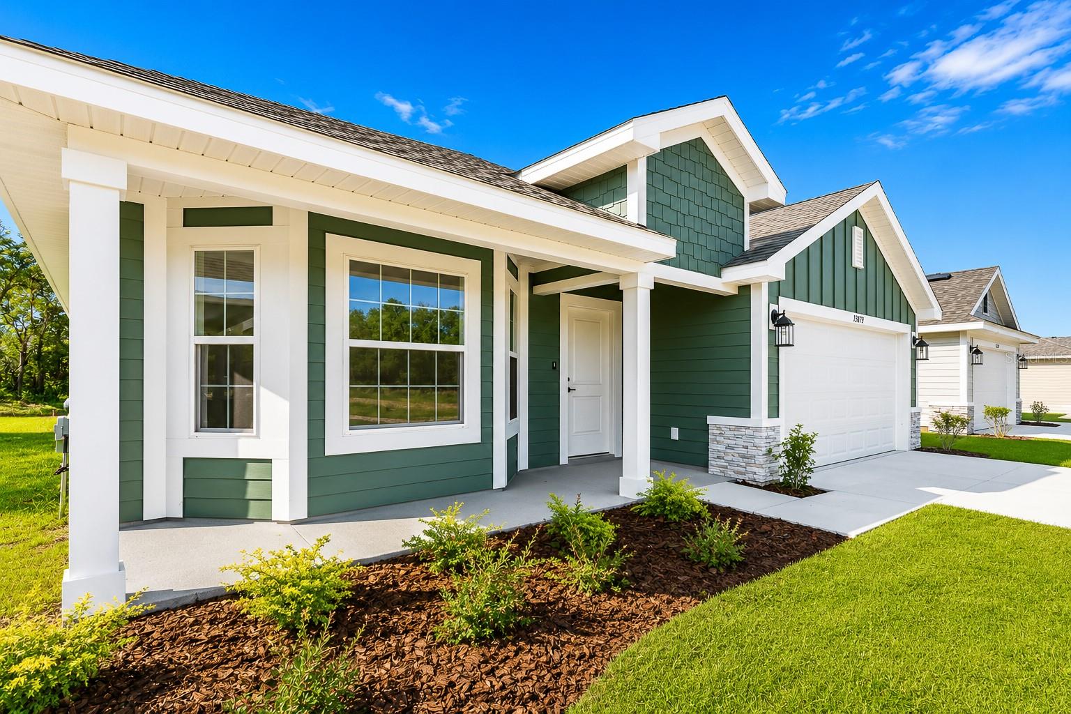 A low-angle exterior view of a green-sided house with white trim, a covered porch, and a garage under a clear blue sky.