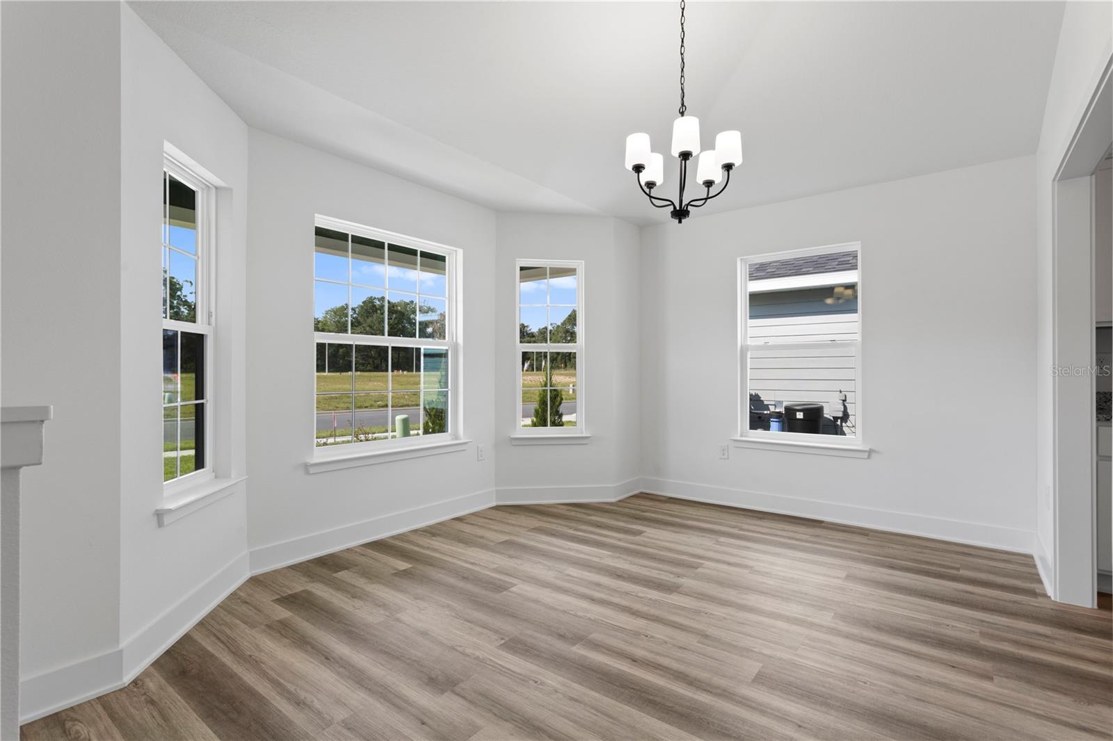 A vacant breakfast nook with light wood-look vinyl flooring, white walls, and a modern chandelier hanging from the ceiling.
