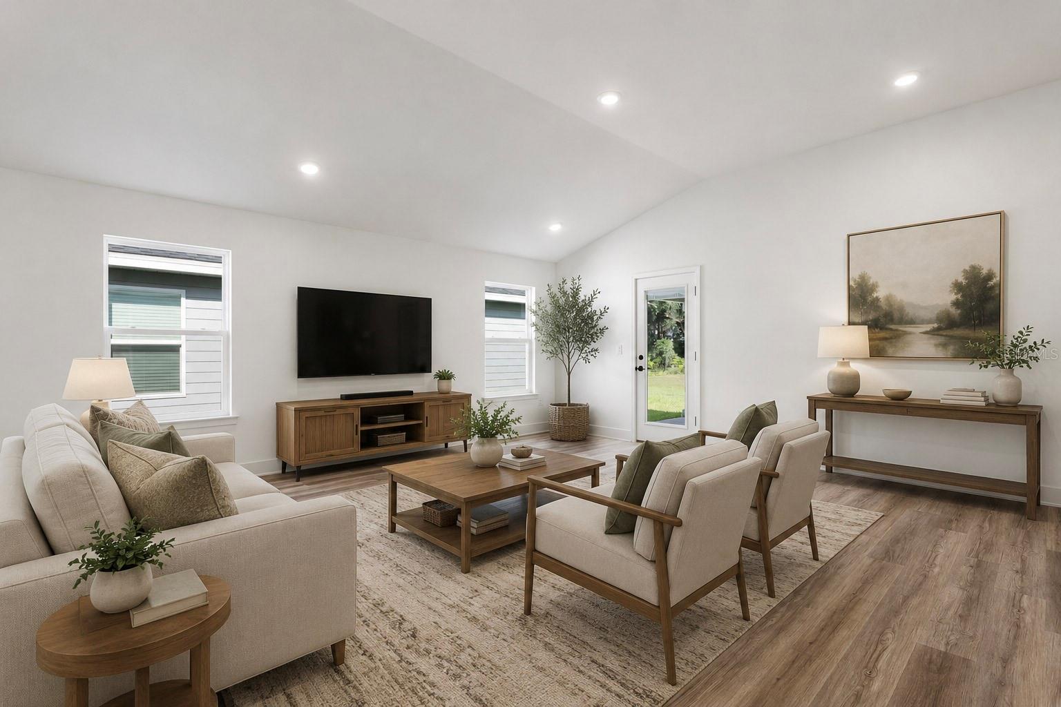 A well-lit, modern living room with a neutral-toned sofa, two armchairs, a coffee table, a wooden media console with a television, and a console table, all arranged on an area rug.