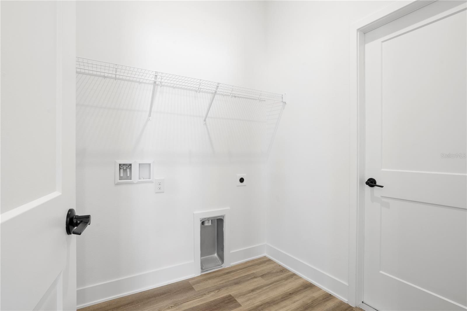 A small white laundry room featuring a wire shelf and wall-mounted connections.