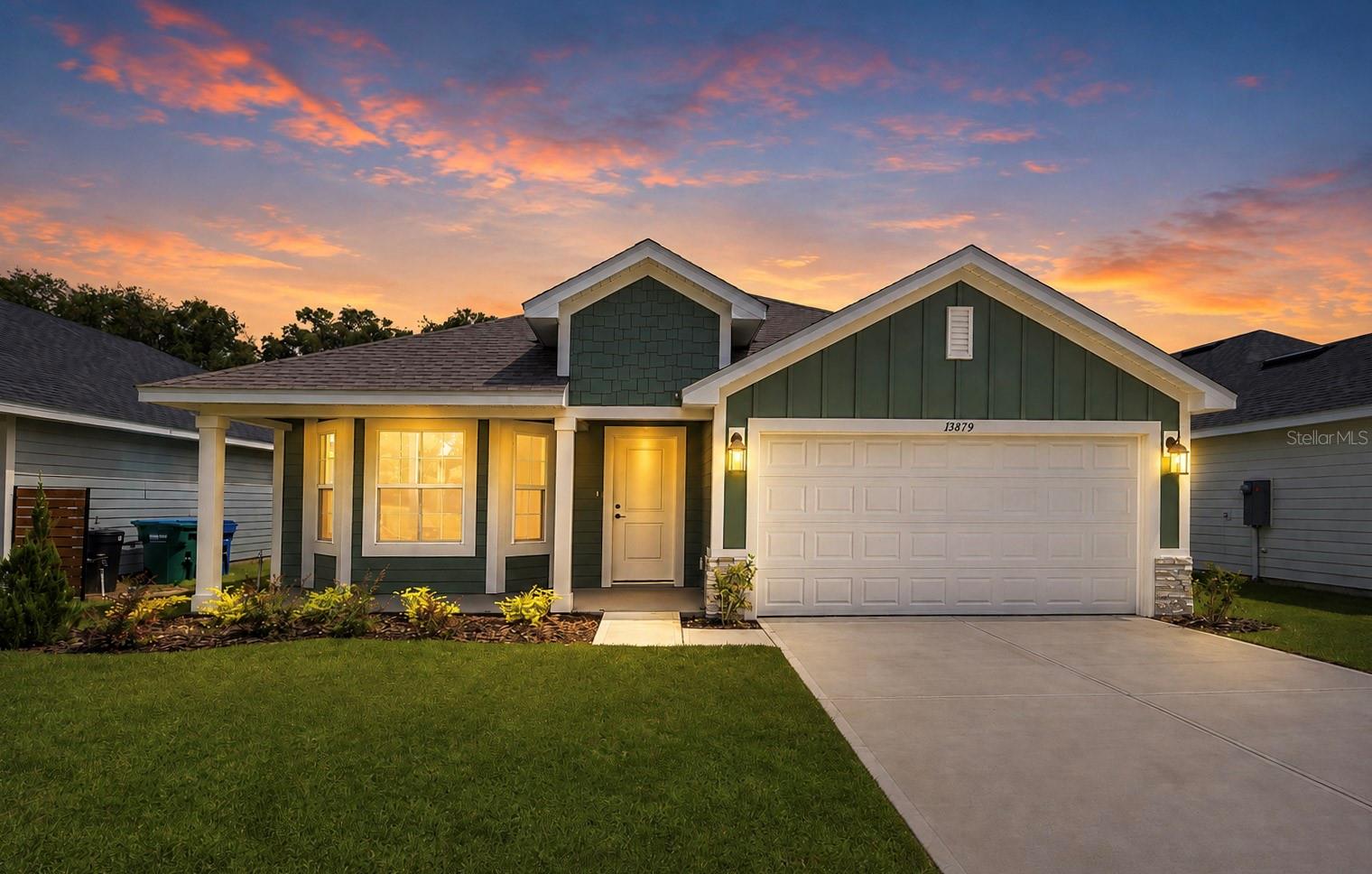 Exterior front view of a single-story home at sunset with a green exterior, white trim, a two-car garage, and a manicured lawn.