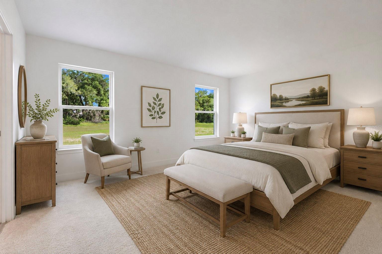 Spacious bedroom featuring neutral tones, an upholstered headboard, matching nightstands, an accent chair by the window, and a landscape view.