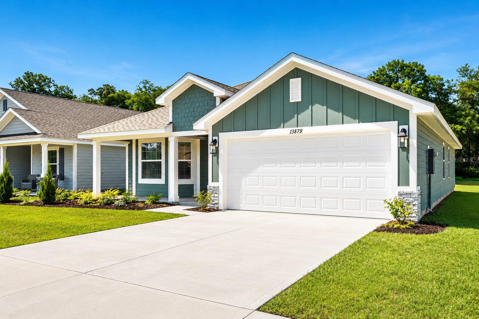 Front exterior of a single-story home with a green board and batten siding, a white double garage, and a manicured lawn.