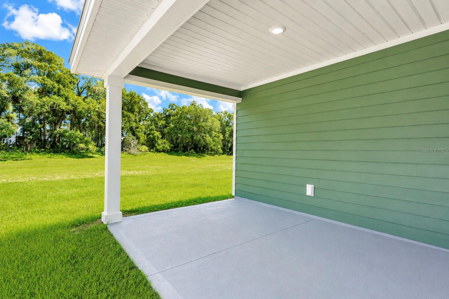 A covered patio with a green wall and a view of a grassy lawn with trees in the background
