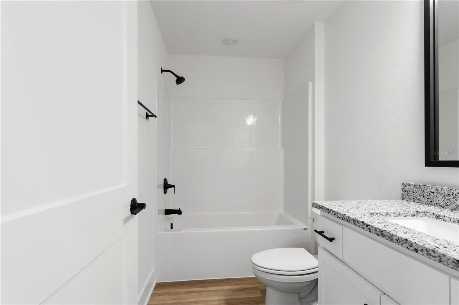 A clean, modern bathroom with white cabinets, a granite countertop, and a white bathtub-shower combo.