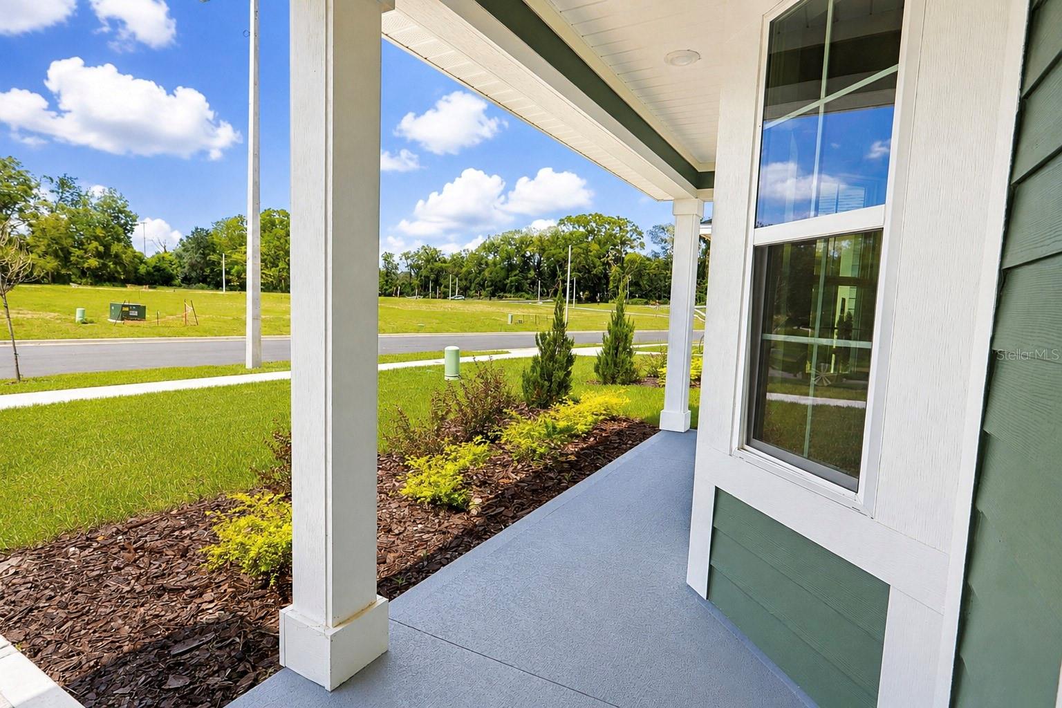 A view from under the covered porch of a house looking out towards a residential street with green lawn and landscaping
