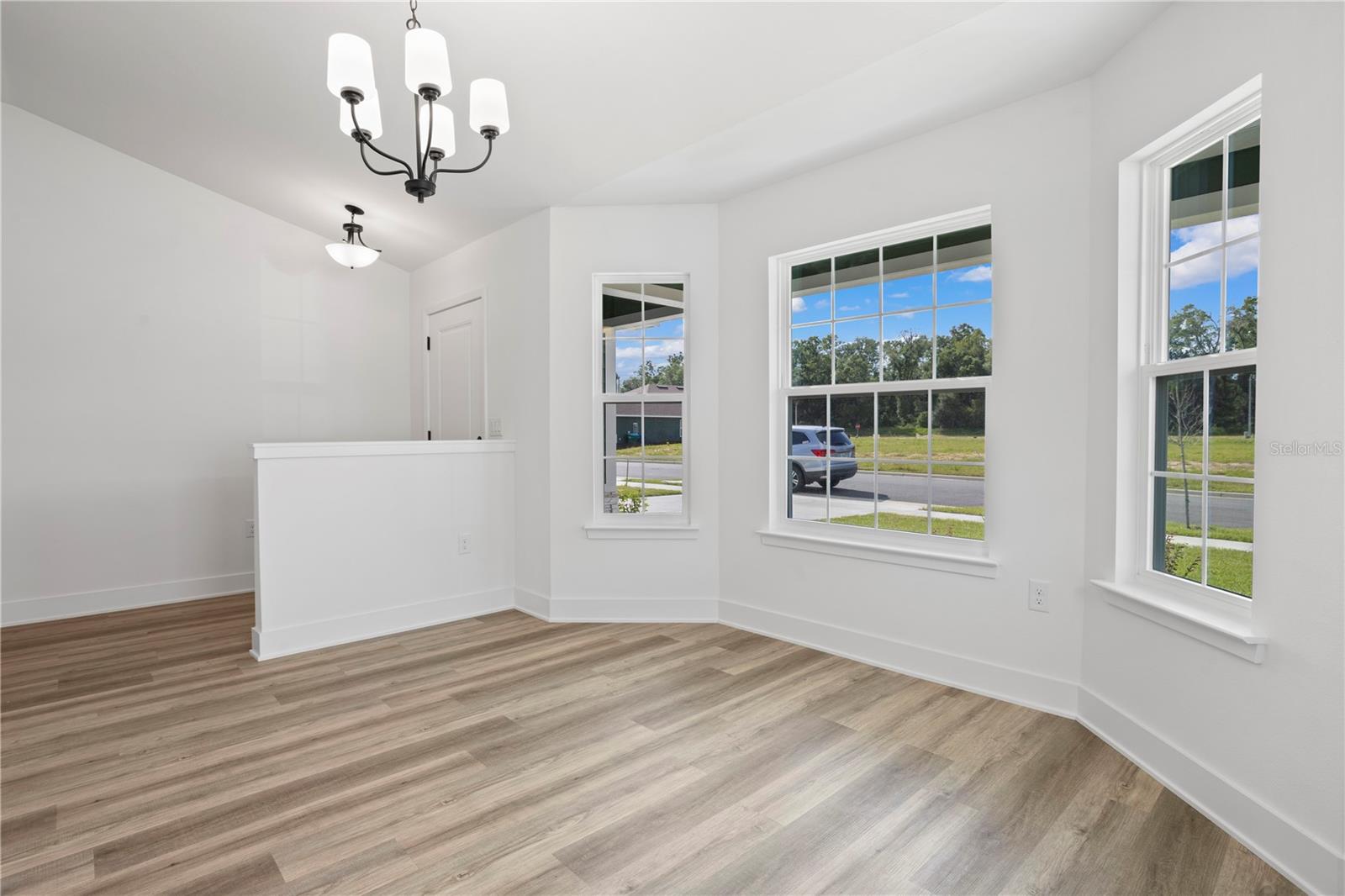 A bright, modern dining area with light wood-look floors, white walls, and a bay window configuration.