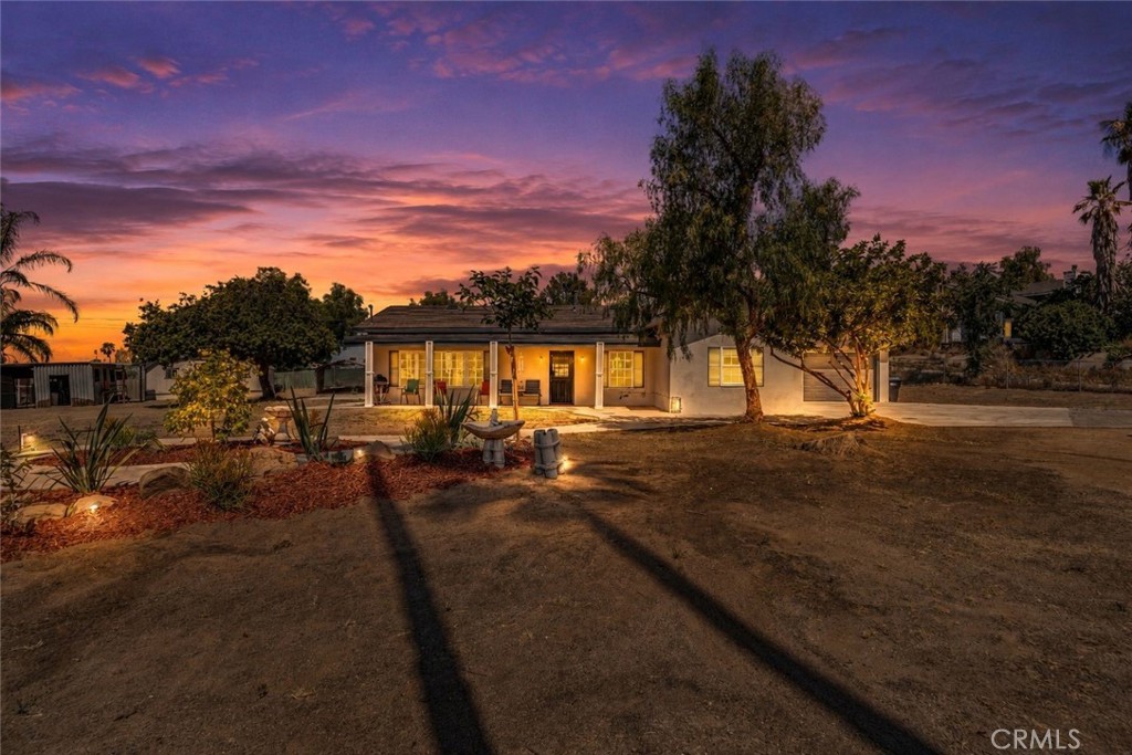Single-story home with a warmly lit front porch and landscaped yard beneath a vivid sunset sky.