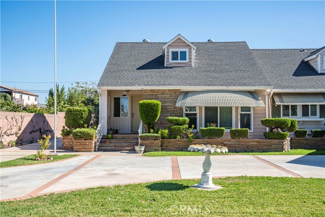 Single-story stone-front home with a gray shingle roof, landscaped front yard, and wide paved driveway.