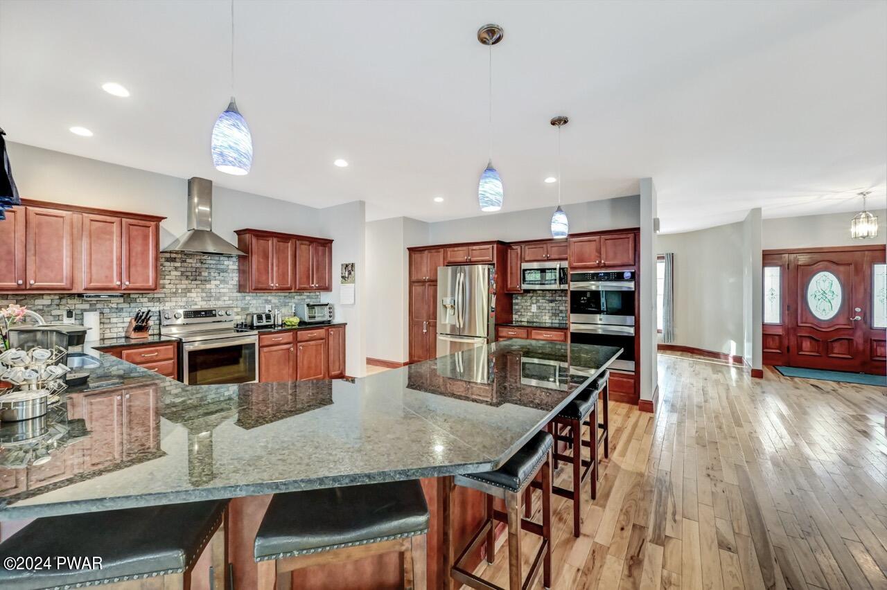 Bright open kitchen with large granite island, cherry cabinets, stainless steel appliances, and hardwood floors near the front entry.