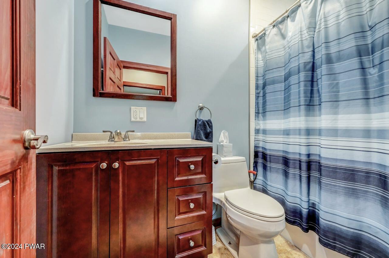 Small bathroom with dark wood vanity, sink, mirror, toilet, and blue striped shower curtain.