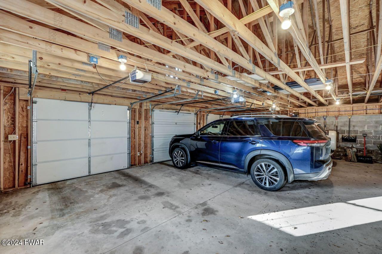 Unfinished two-bay garage with exposed framing, concrete floor, and a blue SUV parked inside.