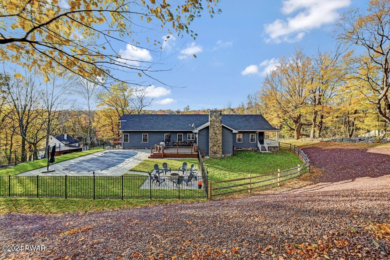Exterior view of a house with a fenced yard, patio seating, and a pool area surrounded by autumn trees.