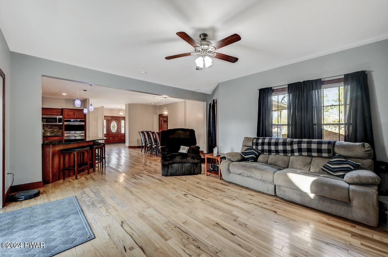Spacious living room with hardwood floors, gray walls, ceiling fan, sofa, recliner, and an open view into the kitchen and dining area.