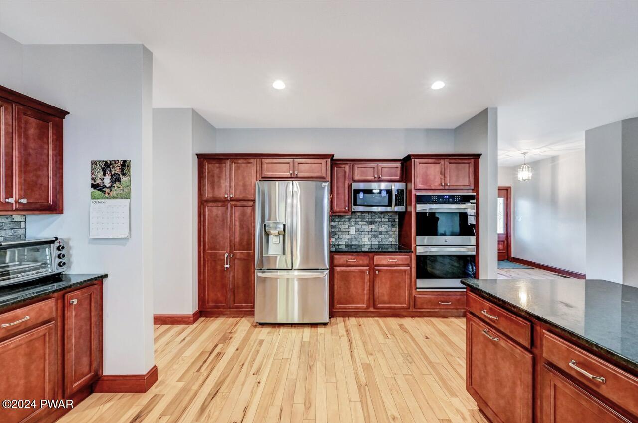 A bright kitchen with hardwood floors, cherry wood cabinets, stainless steel refrigerator and wall oven, and a dark countertop island.