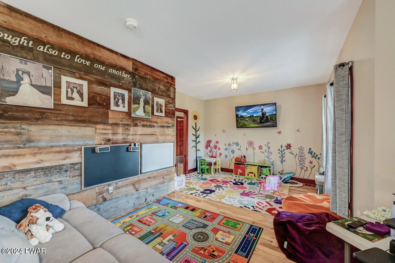A bright playroom with children's rugs, toys, wall flower decals, and a rustic wood accent wall with framed photos.