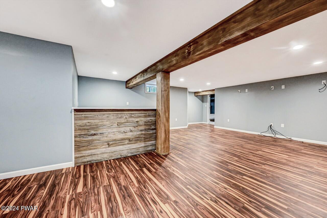Finished basement recreation room with wood-look flooring, gray walls, recessed lighting, and exposed wooden support beams and post.