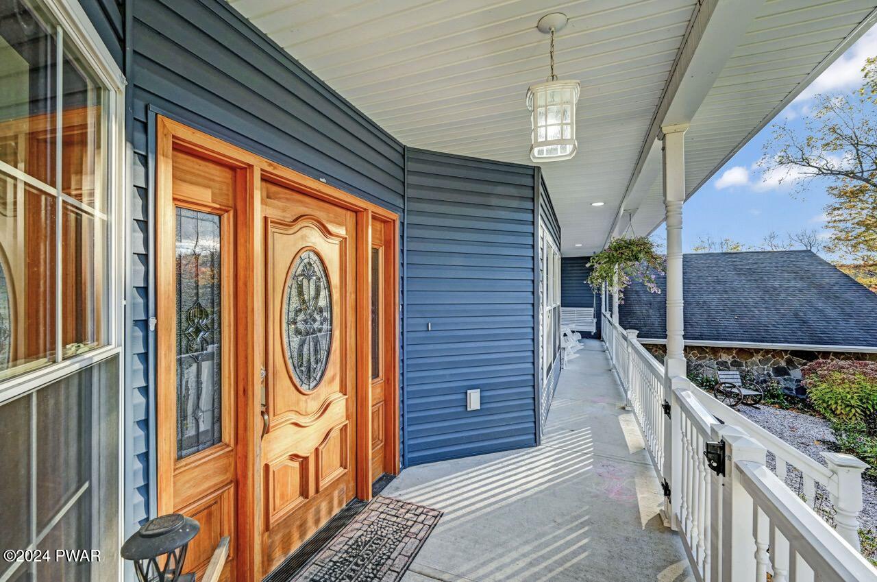 Covered front porch with a decorative wooden front door, blue siding, white railing, and hanging lantern light.