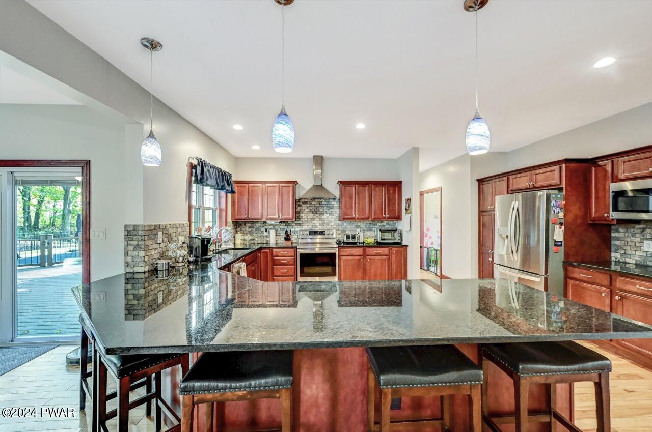 Bright kitchen with cherry wood cabinets, stainless steel appliances, dark granite island, pendant lights, and a doorway to an outdoor deck.