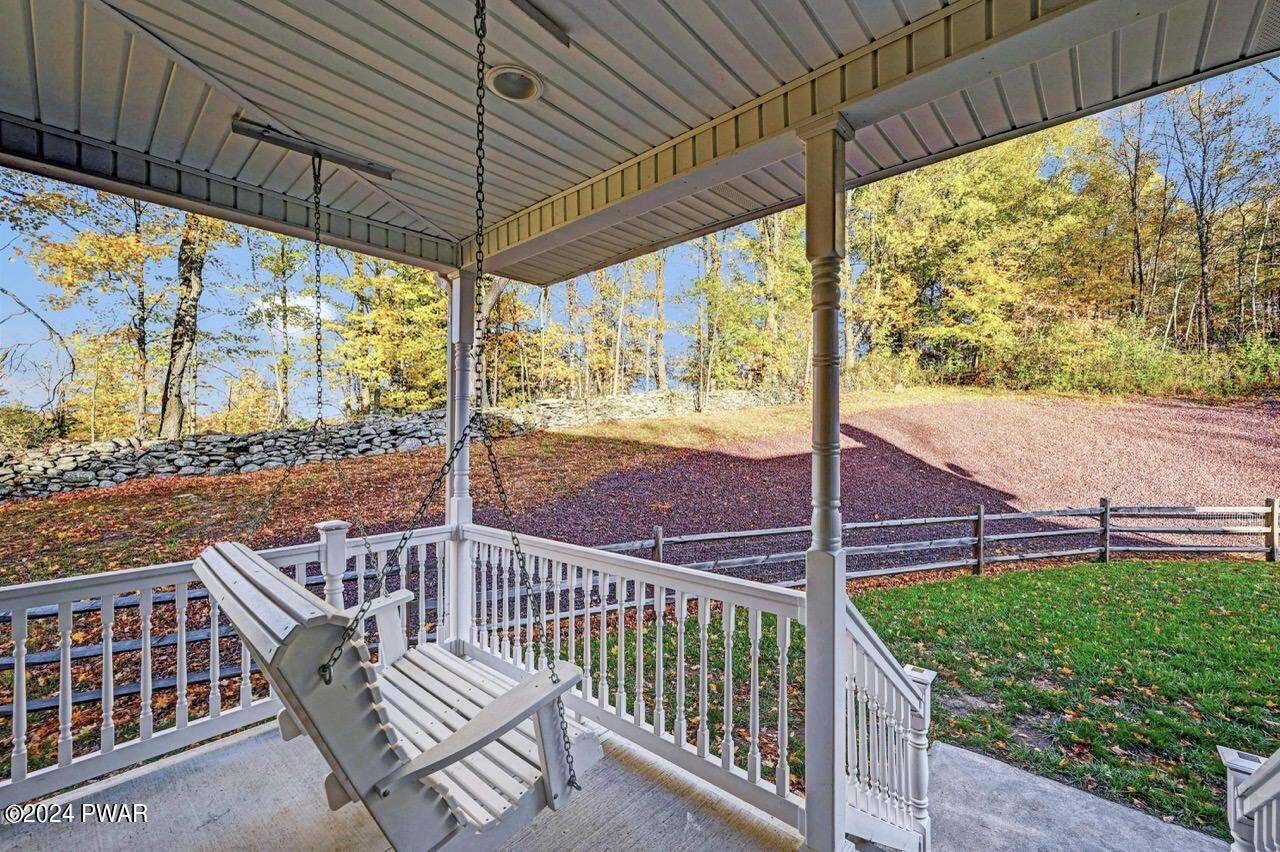 Covered porch with a hanging swing, white railings, and a view of a grassy yard and wooded hillside beyond.