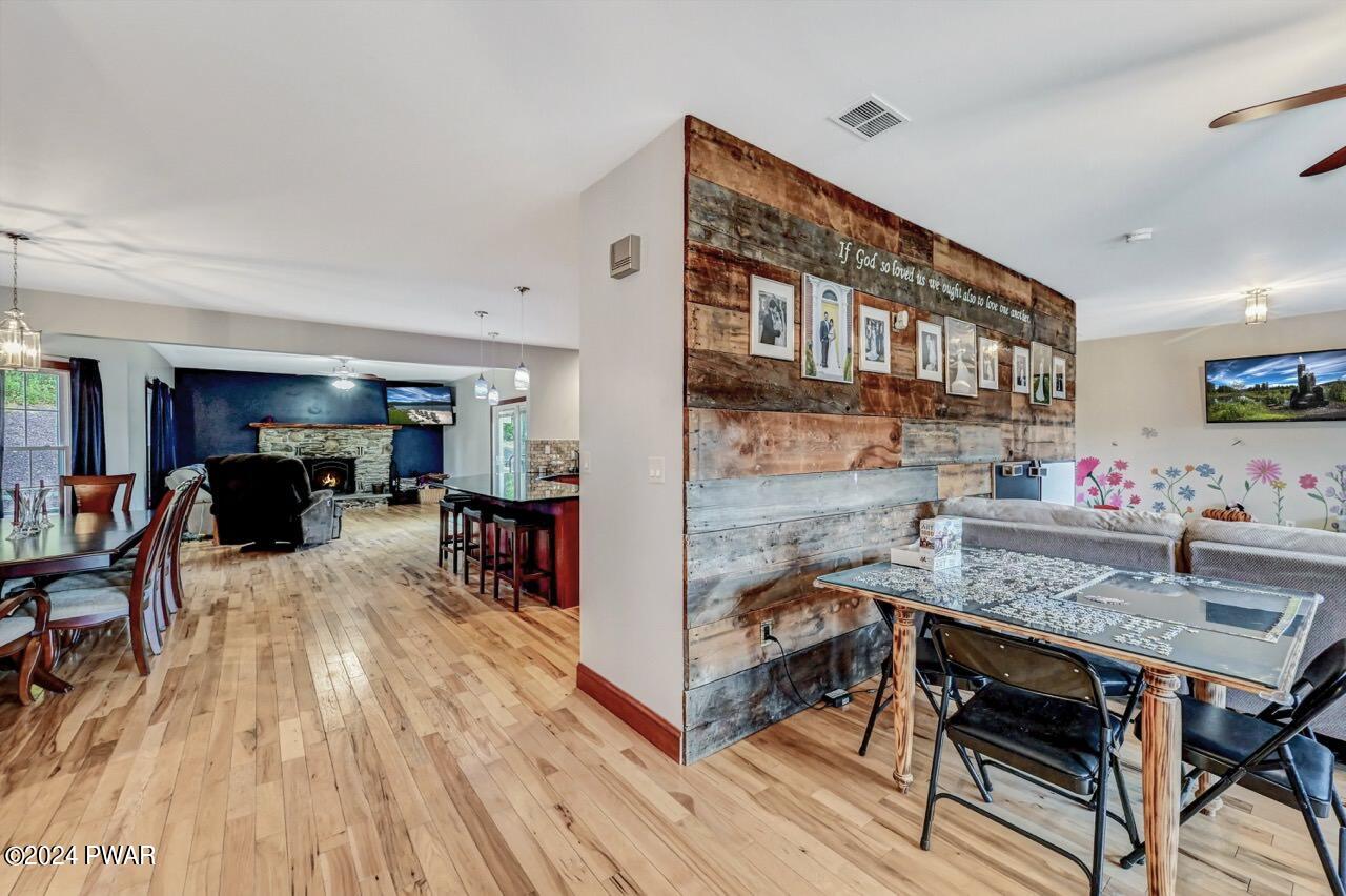 Open-concept interior with hardwood floors, dining area, living room with a stone fireplace, and a rustic wood accent wall.