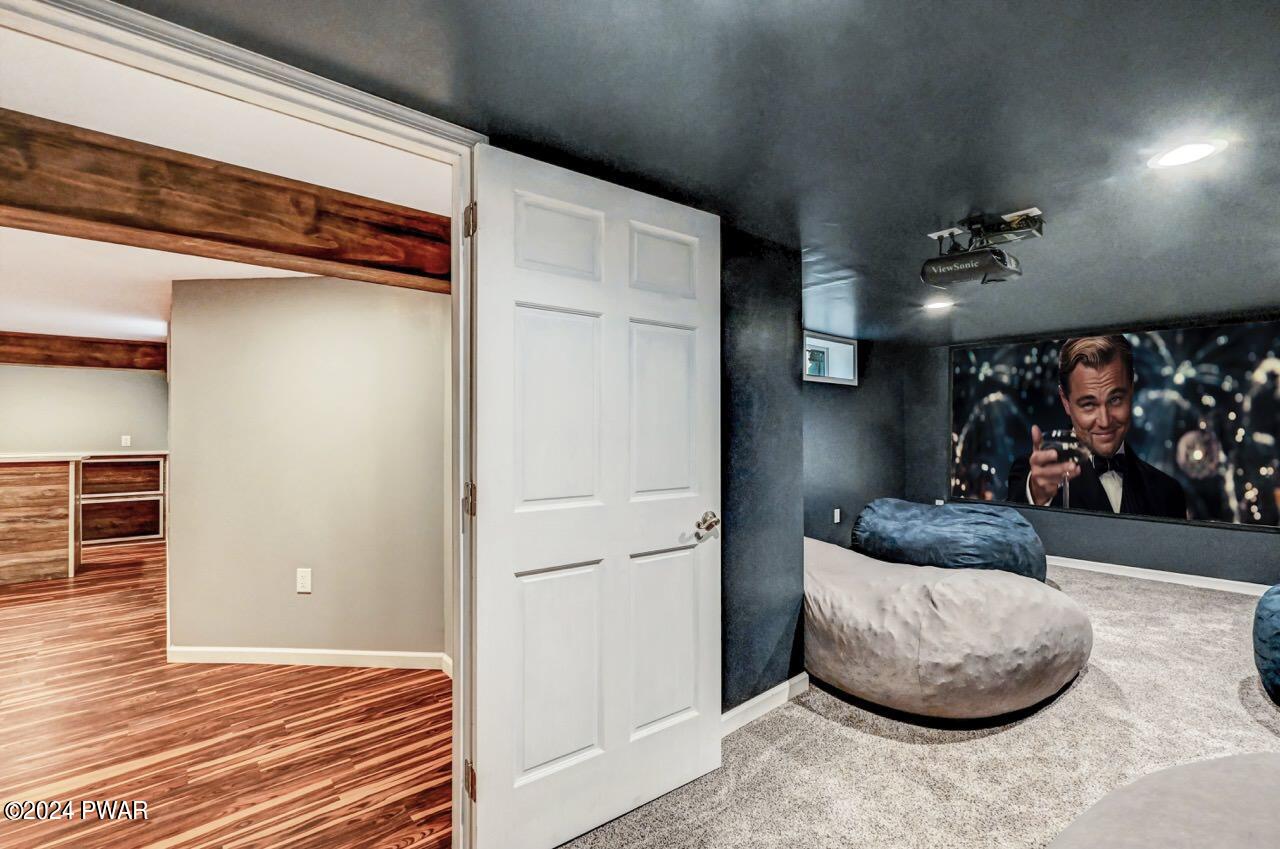Finished bonus room with dark walls, carpet, projector, and large wall screen; adjacent room with wood floors visible through open doorway.
