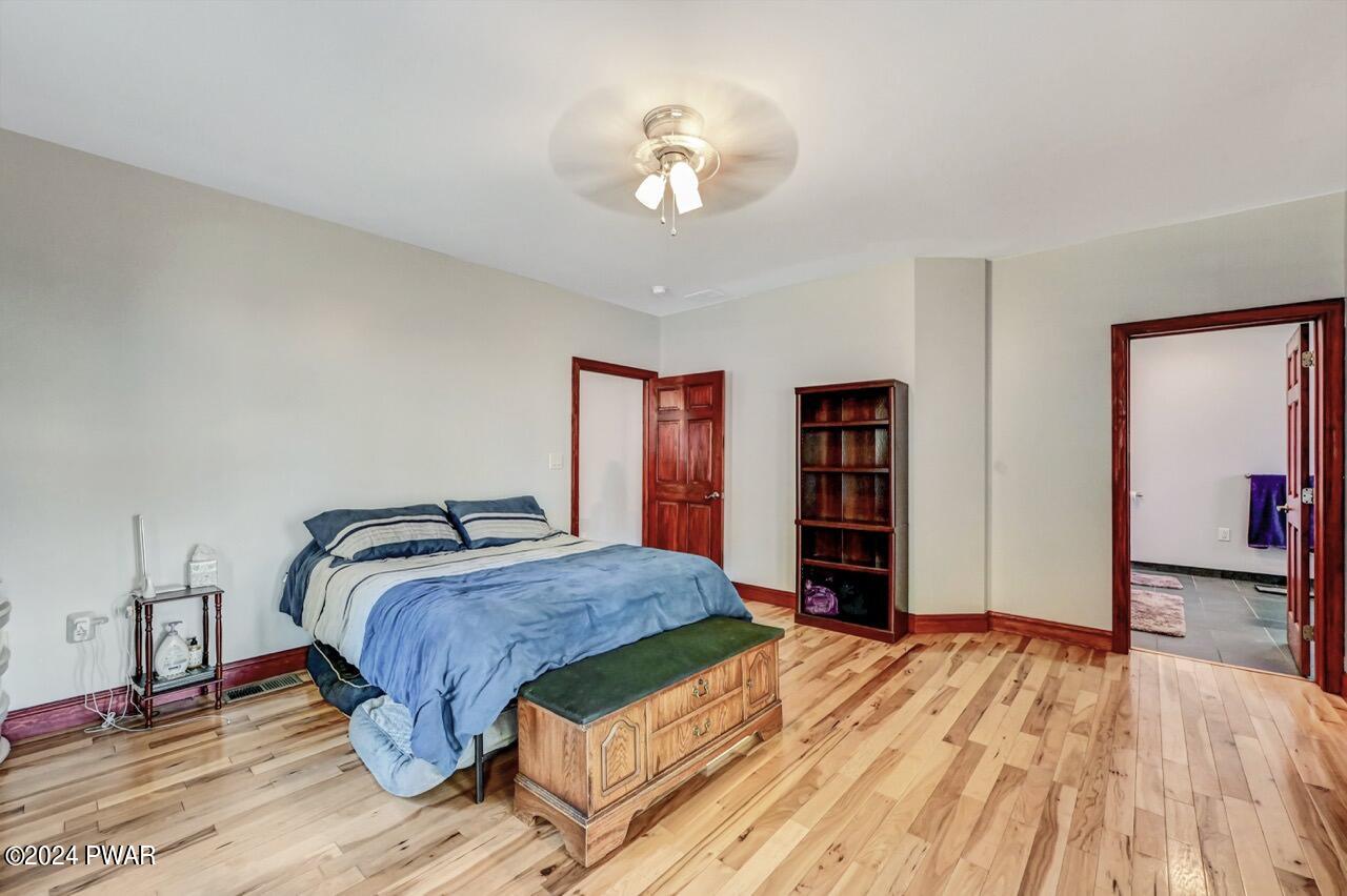 A furnished bedroom with a bed, nightstand, bookshelf, wood floors, and an open doorway to an adjacent bathroom or closet area.