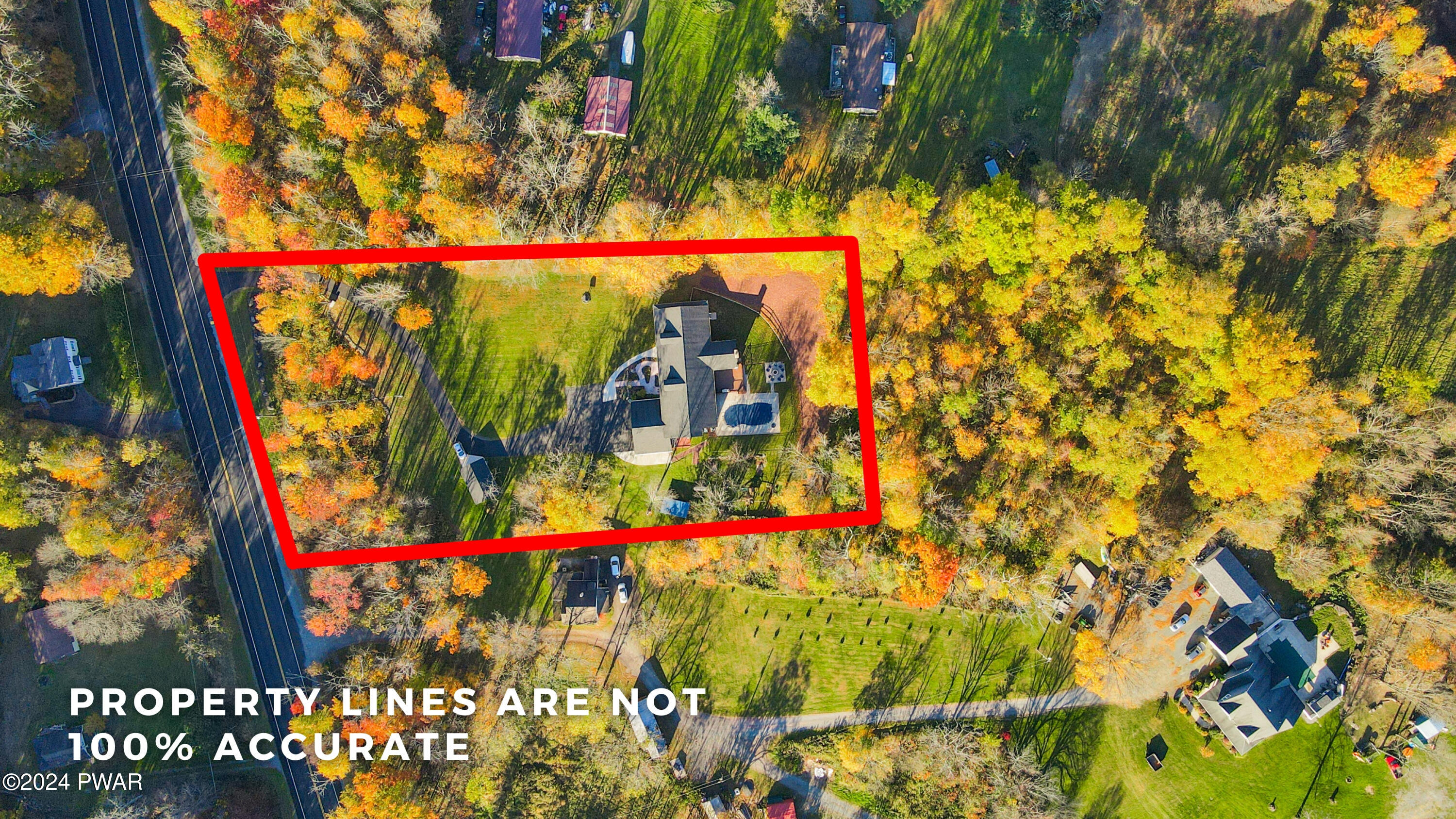 Aerial drone view of a house surrounded by trees and neighboring homes, with a red outline marking the property lines.