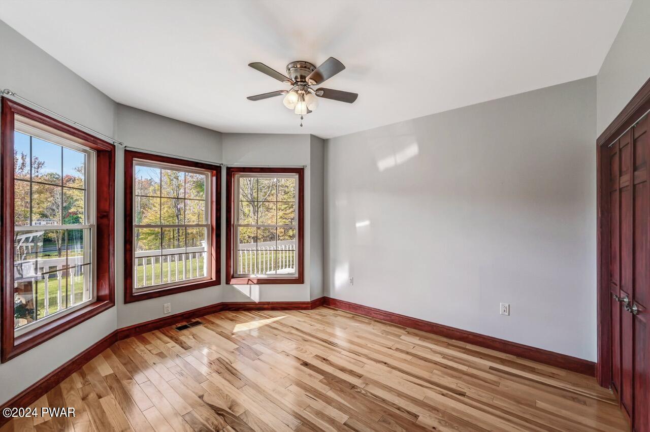 Empty bedroom with bay windows, light gray walls, wood floors, and a ceiling fan.