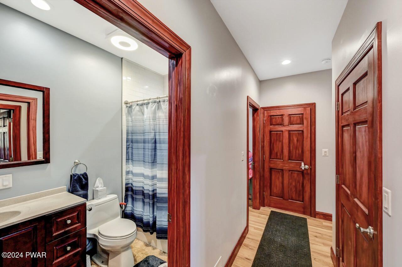 A hallway with wood doors and a glimpse into a bathroom containing a vanity, toilet, and shower curtain.