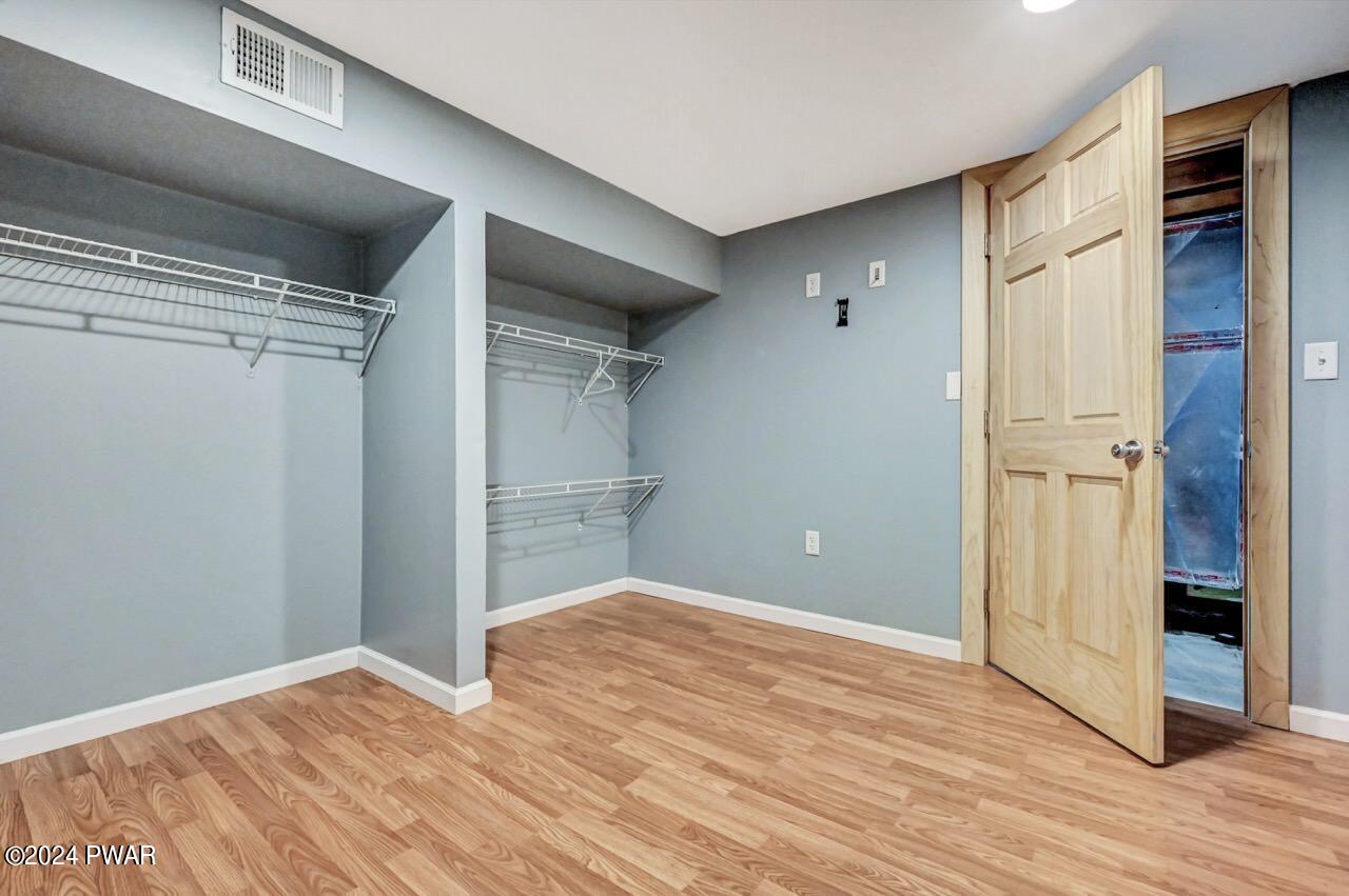 Empty walk-in closet with wire shelving, light blue walls, wood floor, and an open closet door.