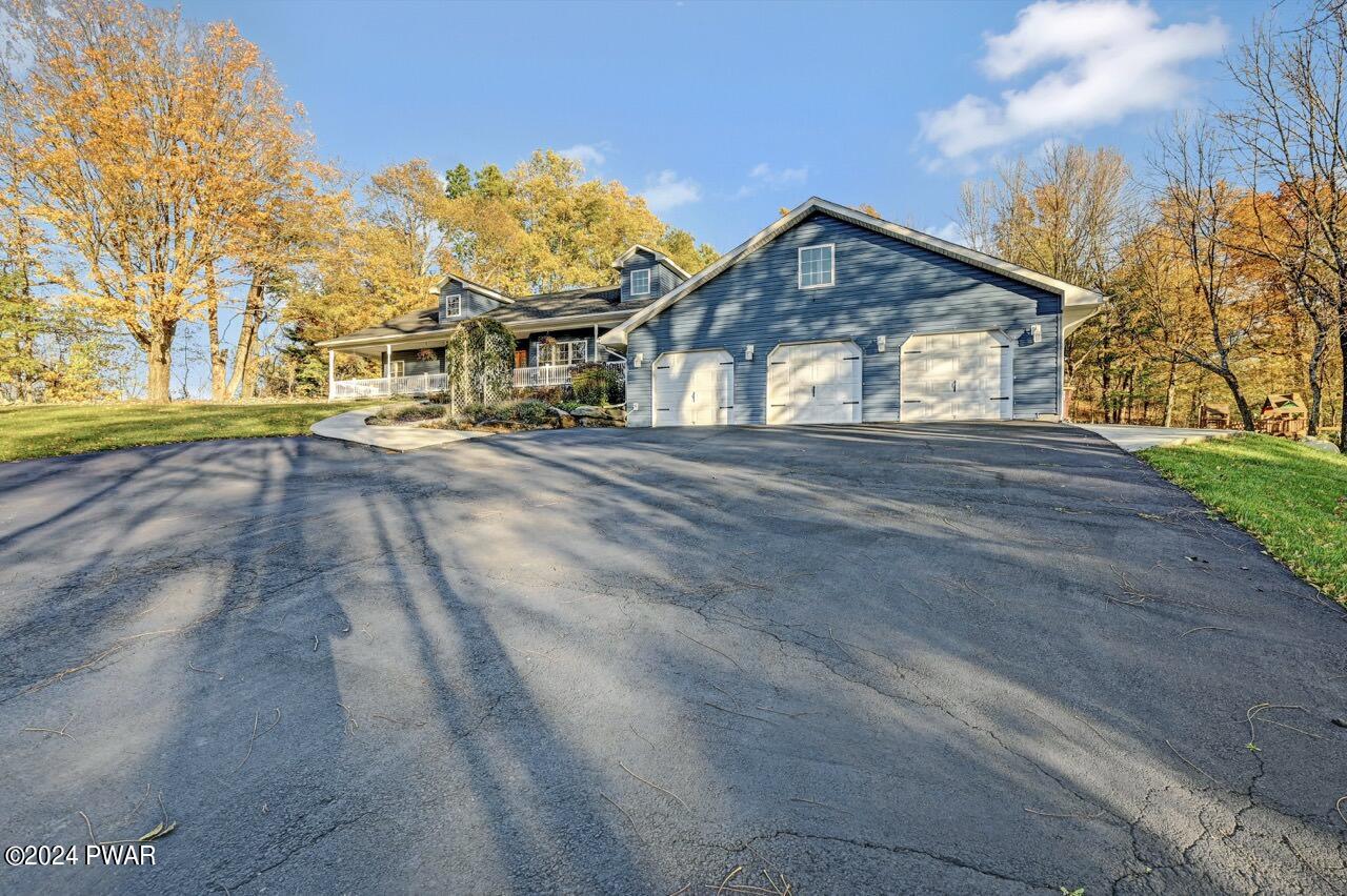 Front exterior of a blue house with a three-car garage, large driveway, and autumn trees surrounding the property.