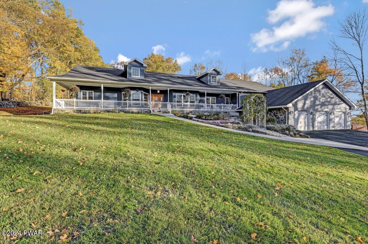 Front exterior of a large single-story house with a covered porch, attached three-car garage, and autumn trees in the background.