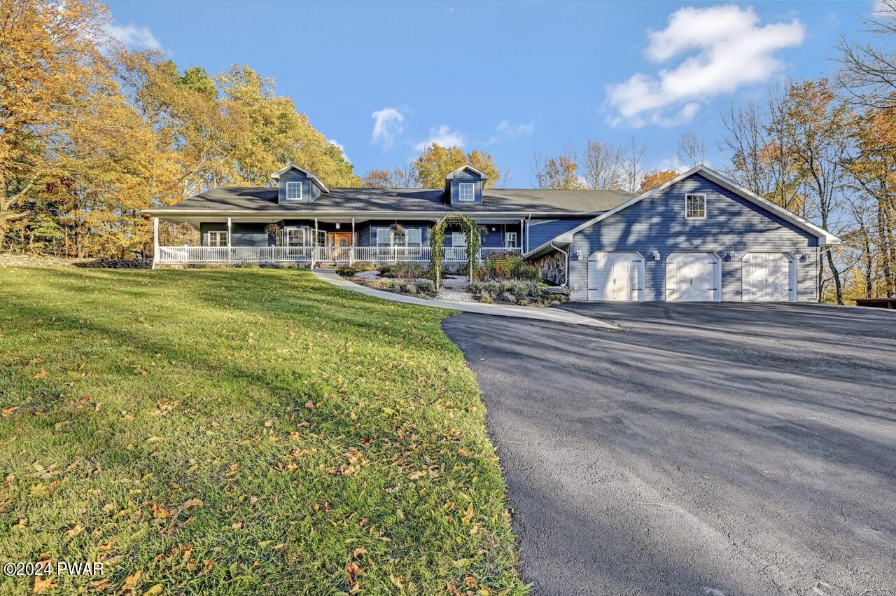 Front exterior of a blue house with a large driveway, attached three-car garage, and covered porch, surrounded by autumn trees.