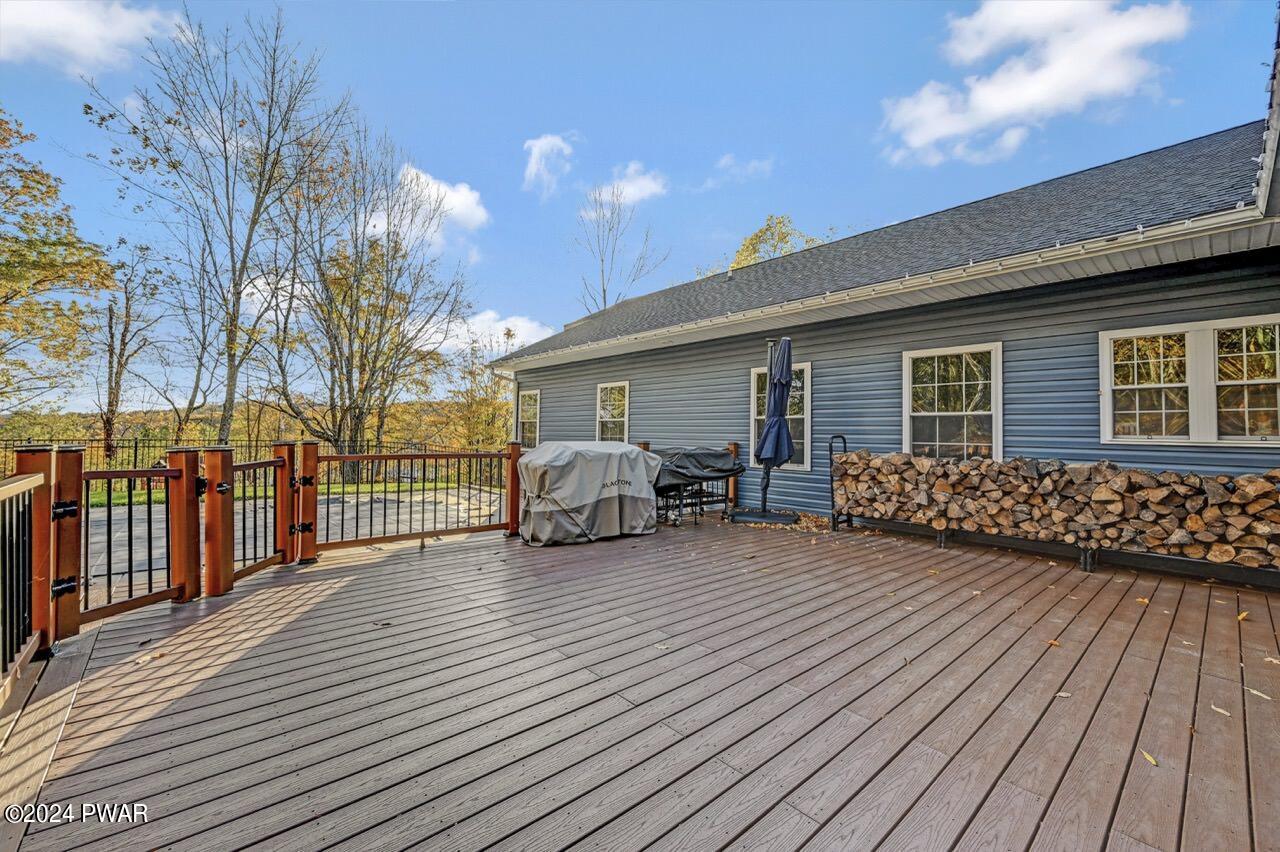 A spacious wooden rear deck with railing, a covered grill, umbrella stand, and stacked firewood along the house exterior.