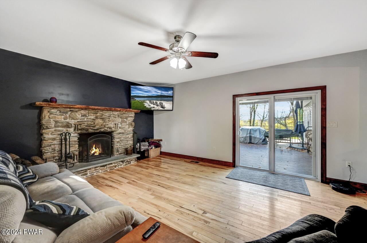Living room with hardwood floors, stone fireplace, ceiling fan, wall-mounted TV, and sliding glass doors to a deck.