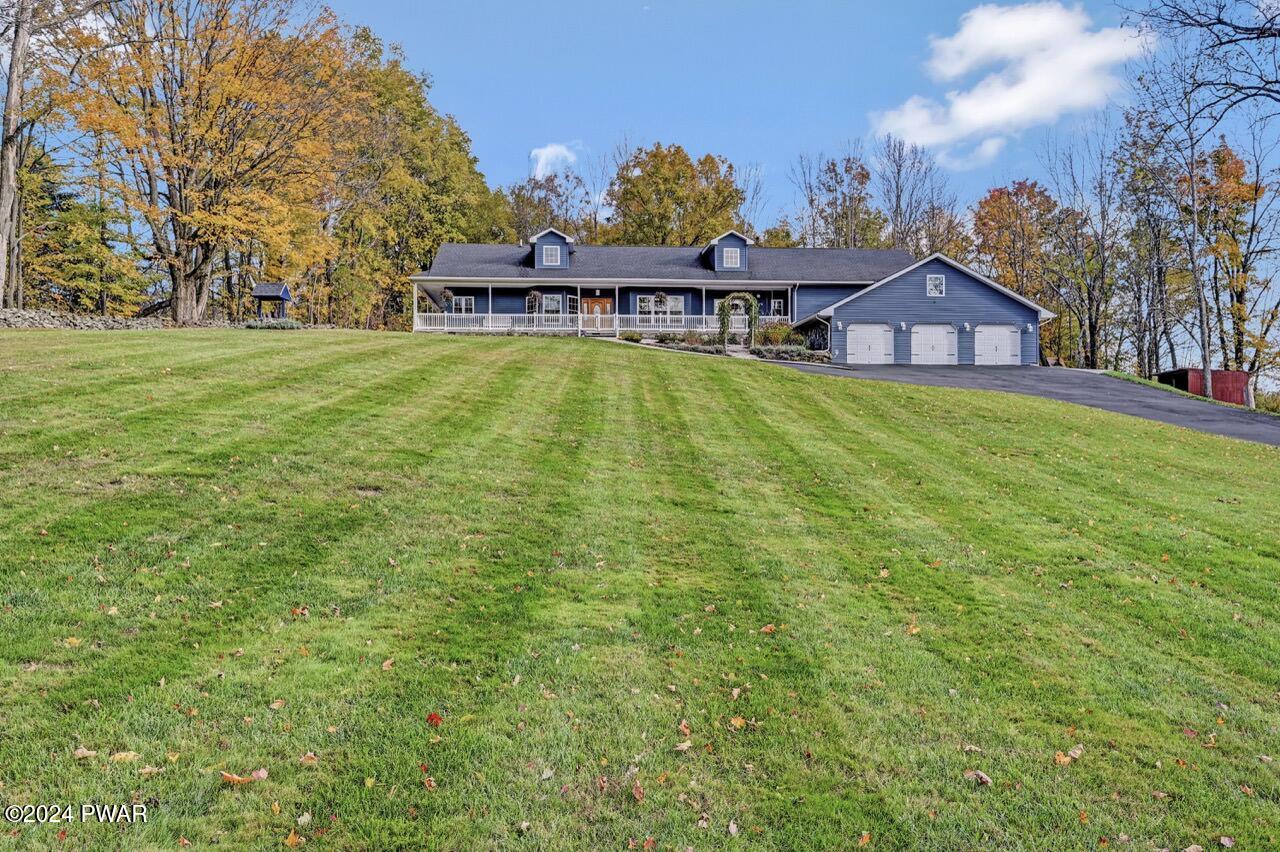 A blue single-family house with a large front lawn, covered porch, attached three-car garage, and autumn trees in the background.